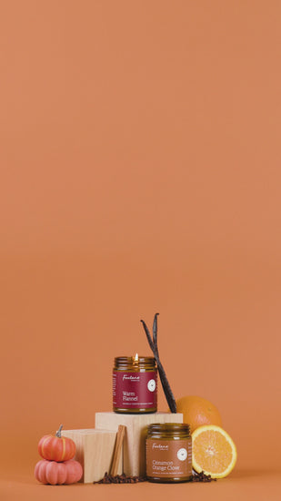 Pumpkin Pie, Warm Flannel and Cinnamon Orange Clove Candle surrounded with vanilla beans, pumpkins, oranges, and cinnamon sticks on an orange background