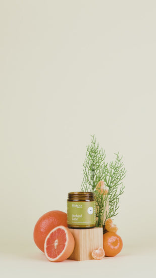 Orchard Lane Candle in a jar with oranges, tangerines and greenery on a beige background