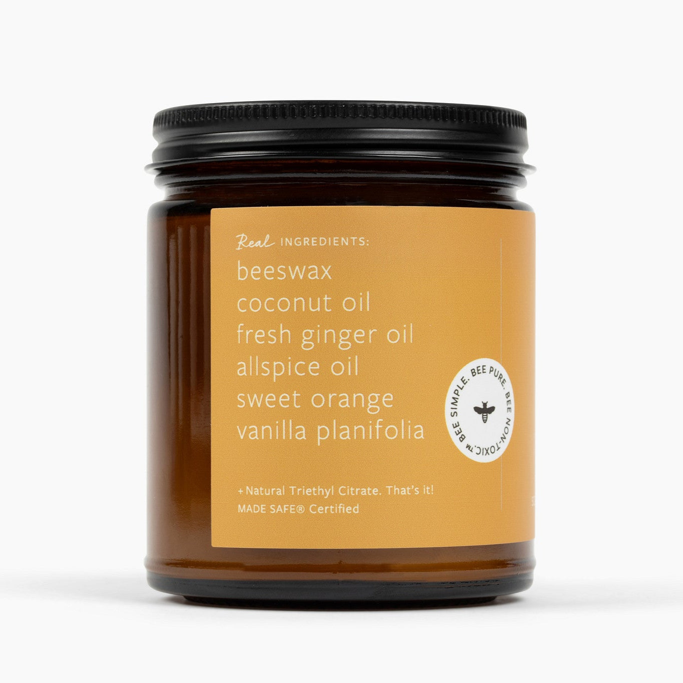 Side of an amber glass jar candle with a golden color label and the ingredients: beeswax, coconut oil, fresh ginger oil, allspice oil, sweet orange, vanilla planifolia, and natural triethyl citrate.