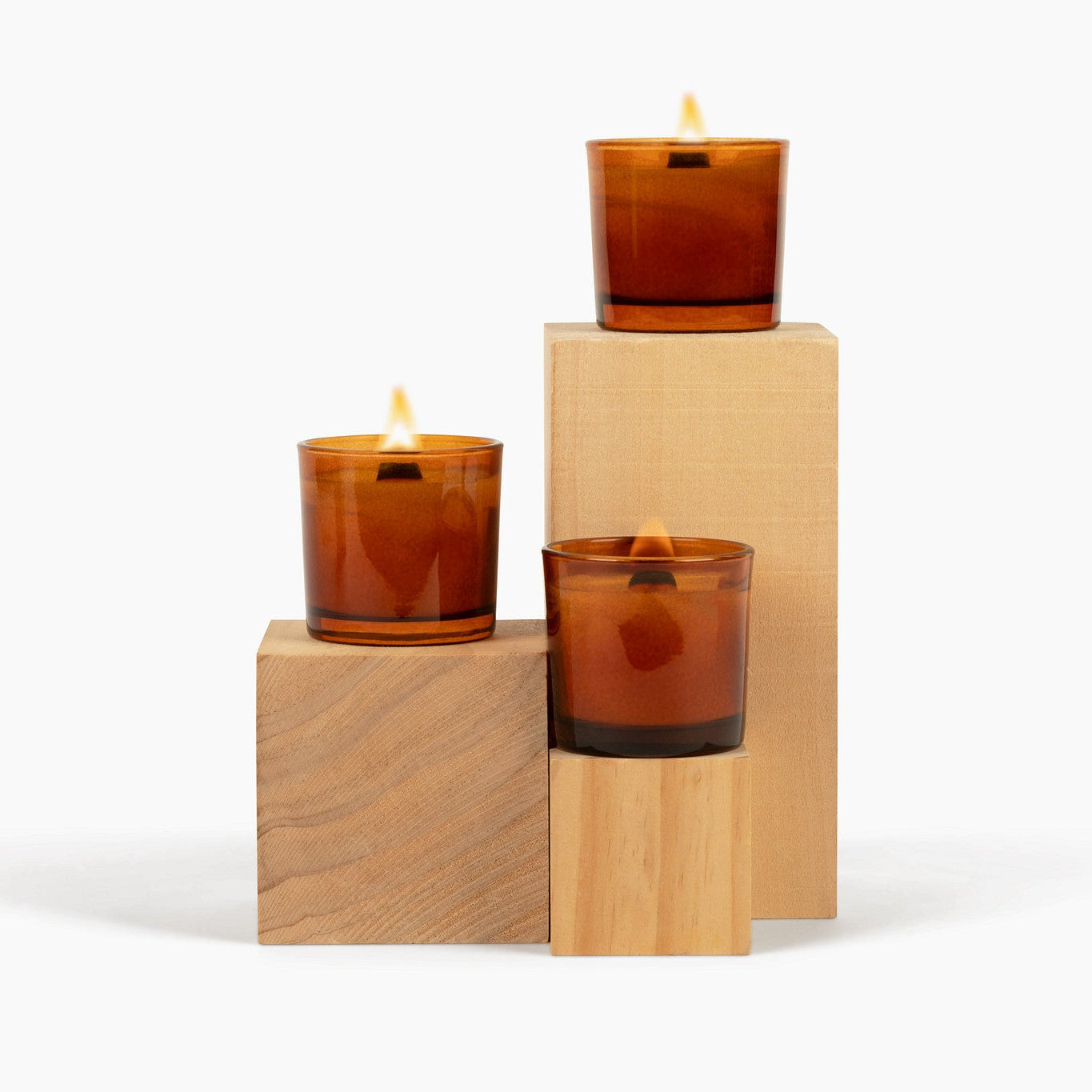 Three amber-colored candles on wooden blocks against a white background