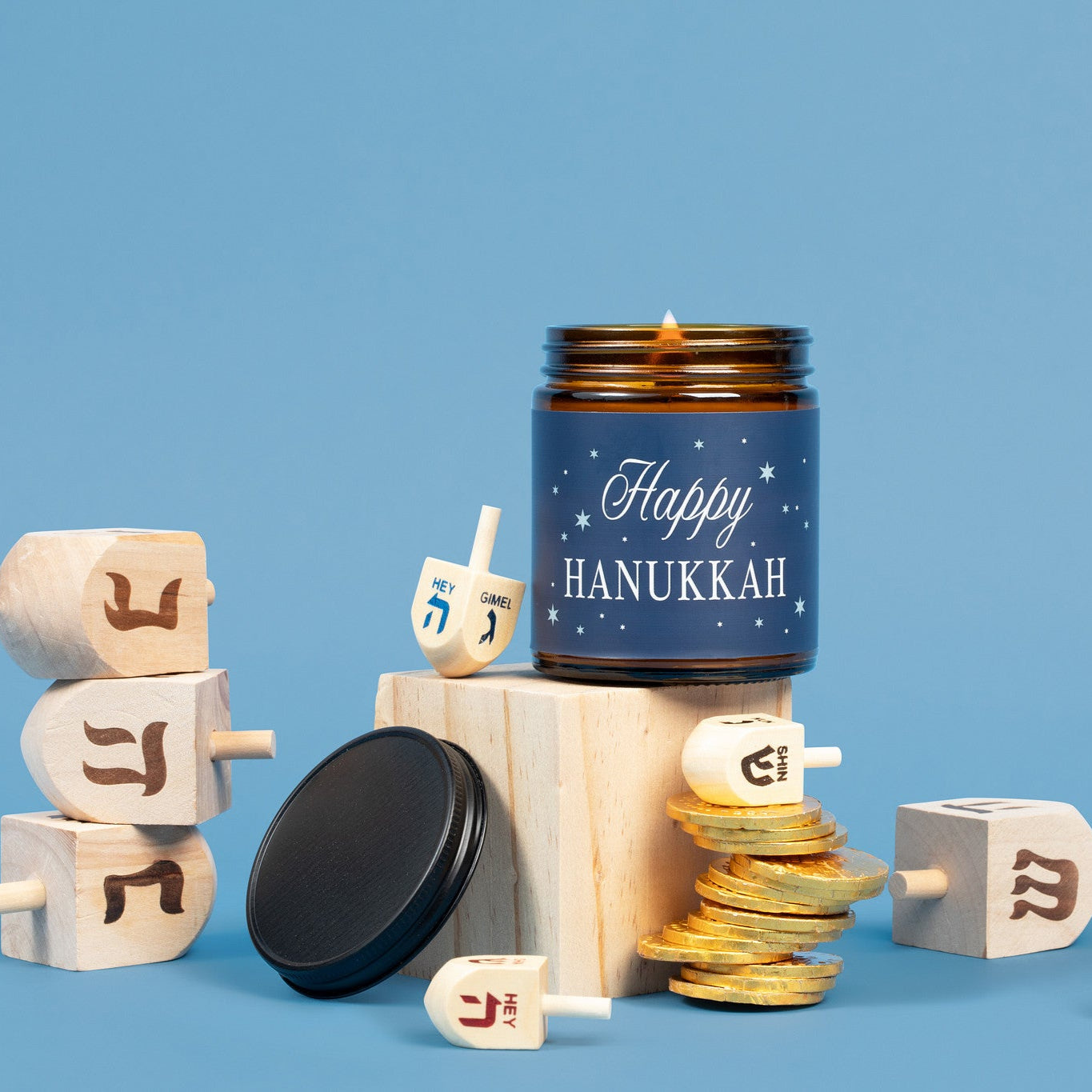 Candle with 'Happy Hanukkah' text surrounded by wooden dreidels on a blue background