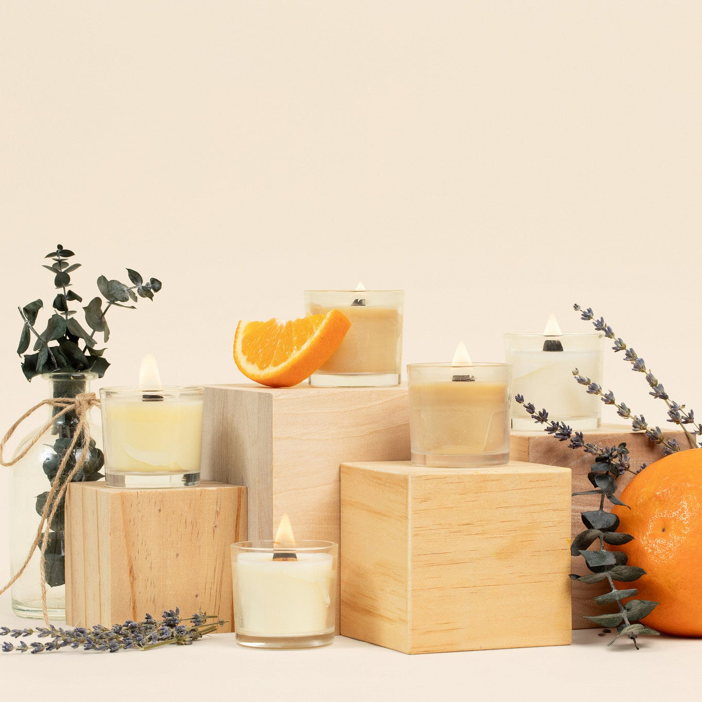Mini glass votive candles on a beige background with oranges, lavender, and eucalyptus. 