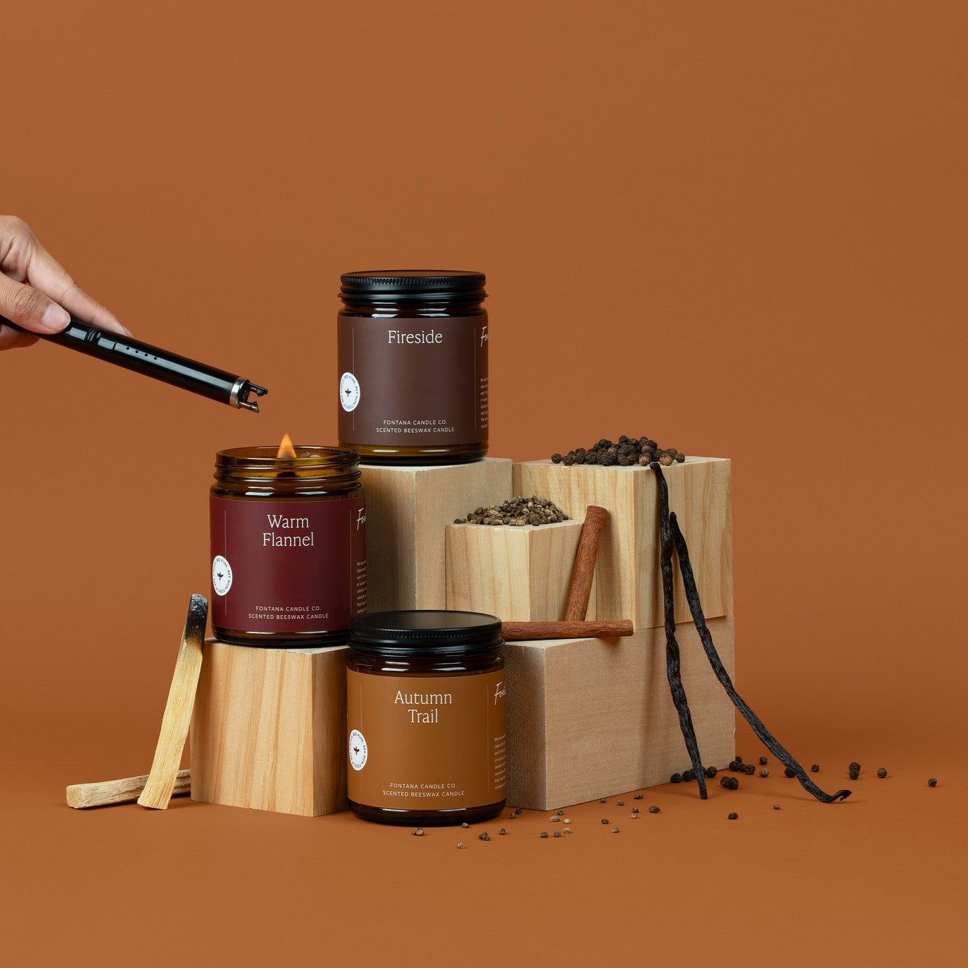 3 amber glass jar candles on a brown background surrounded by oranges, palo santo sticks, cinnamon sticks, and vanilla beans.