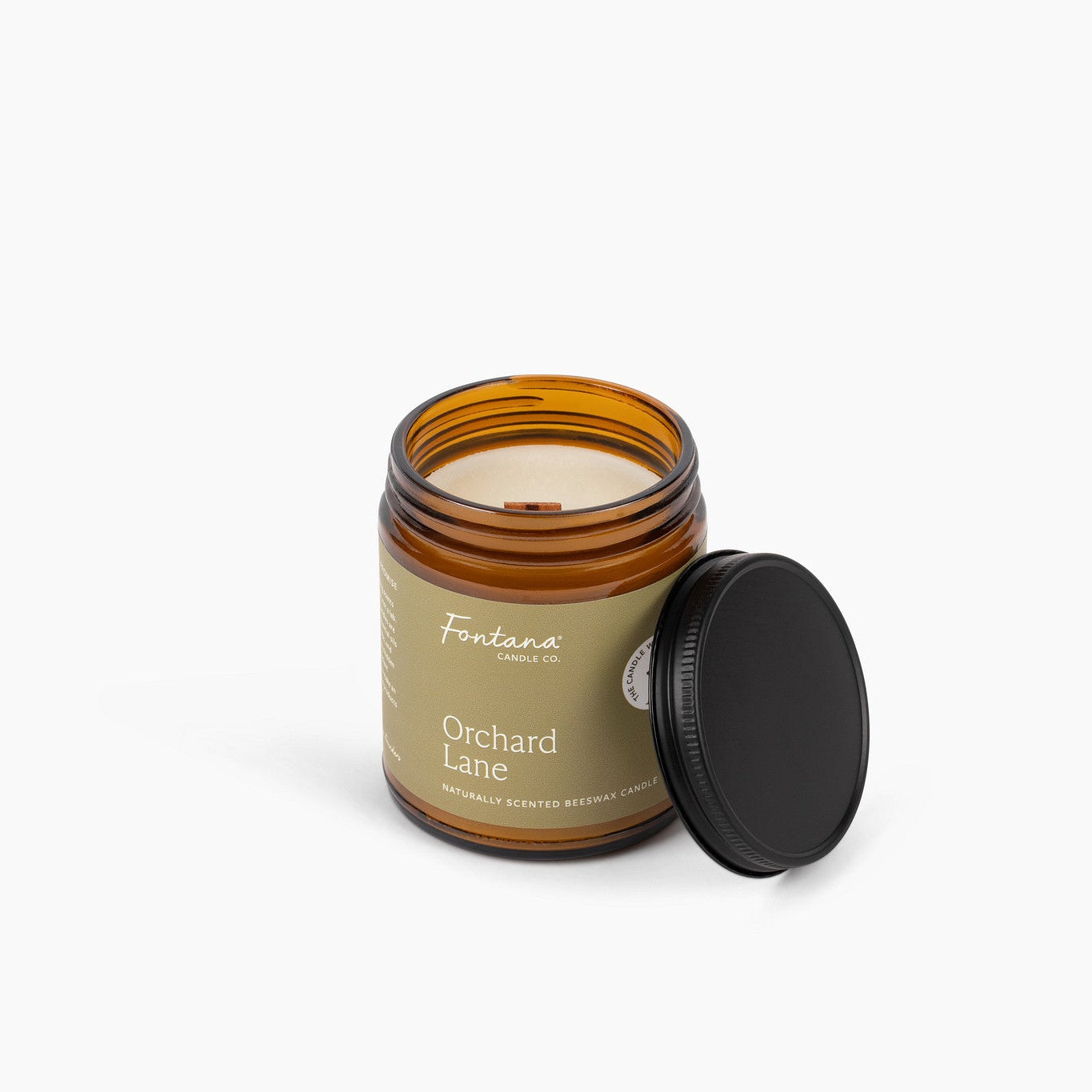Candle in a glass jar with a wooden wick labeled 'Orchard Lane’ on a white background.
