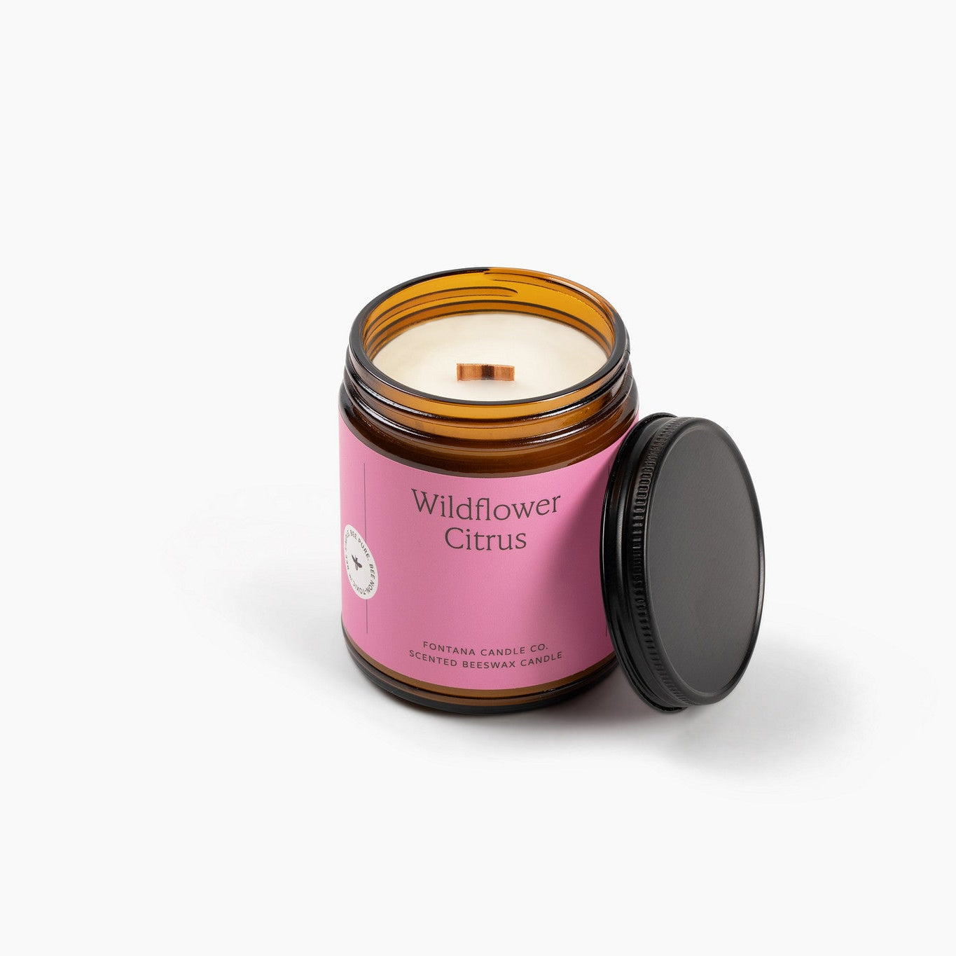 Amber glass jar candle with pink packaging labeled 'Wildflower Citrus' on a white background