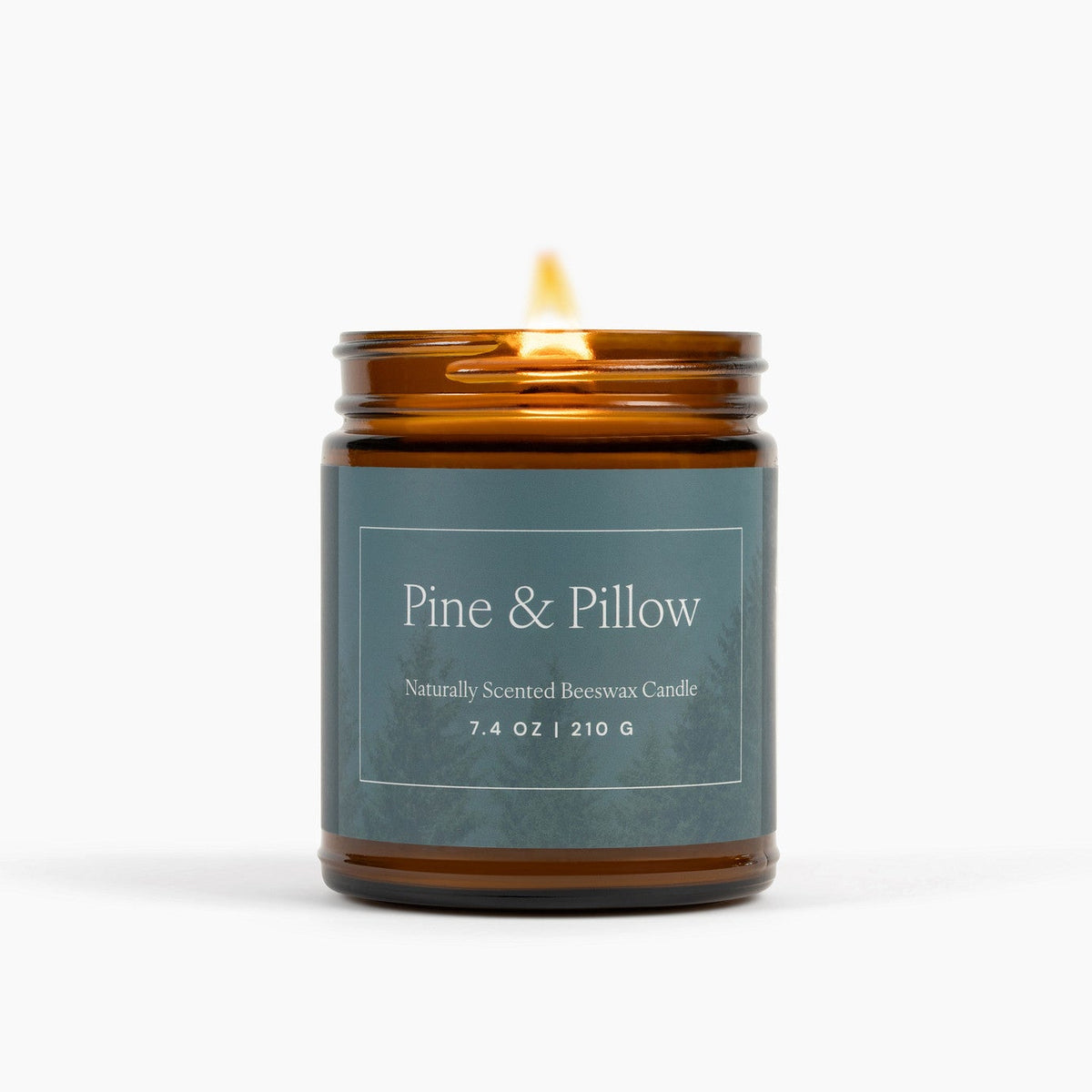 Lit amber glass jar candle with a blue label featuring pine trees in front of a white background.