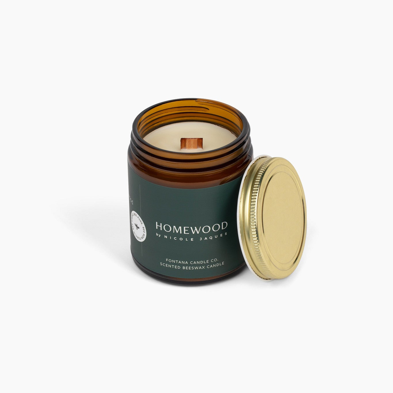 Amber glass jar candle called Homewood, with a dark green label, in front of a white background.