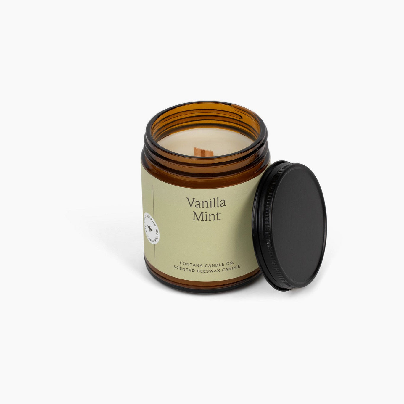 Unlit amber glass jar candle with a light green label, and Vanilla Mint on the front. Candle is in front of a white background.