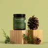 Jar of 'Northern Pine' on a wooden block with pine cones and branches against a green background