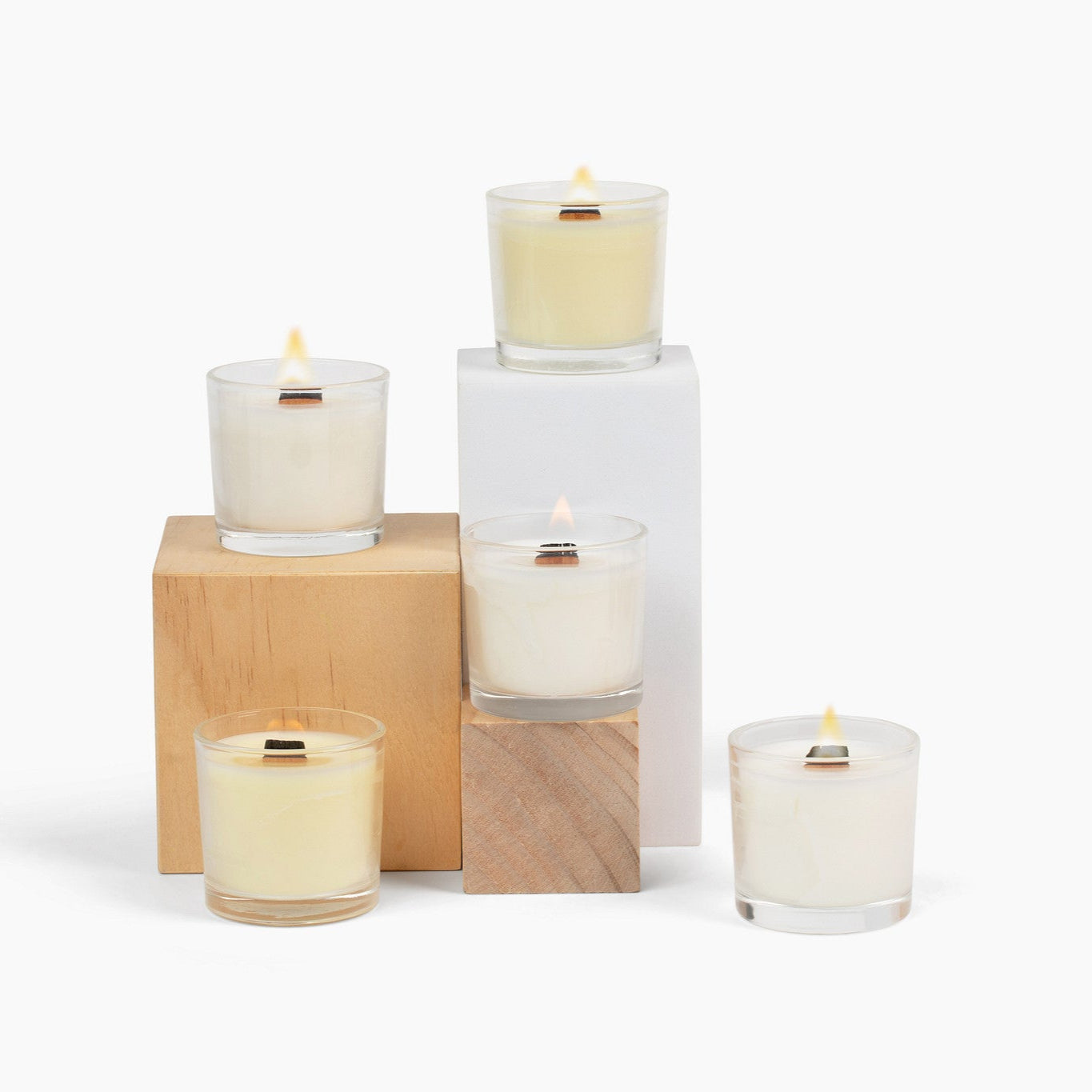 5 lit mini glass candles on wooden blocks, in front of a white background.