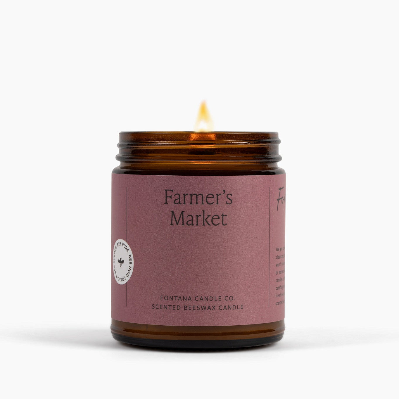 Lit amber glass jar candle with 'Farmer's Market' label on a white background.