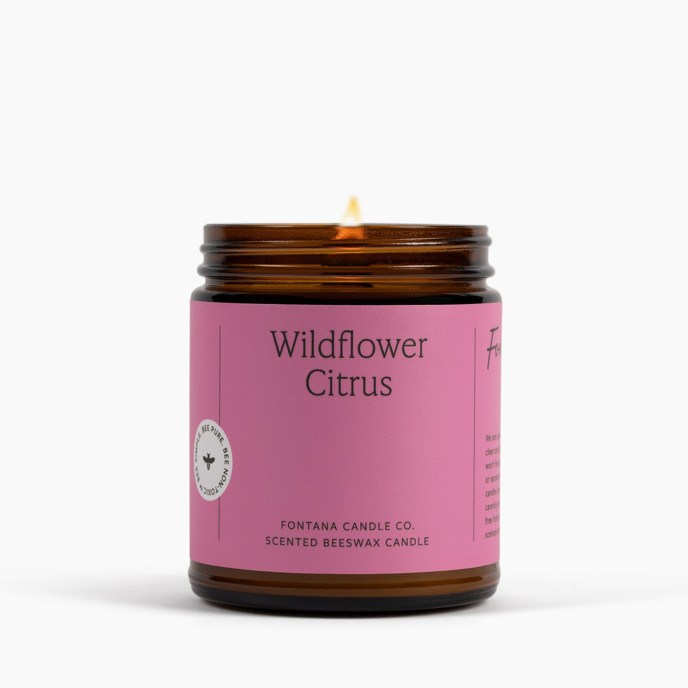 Lit amber glass candle with a pink label on a white background