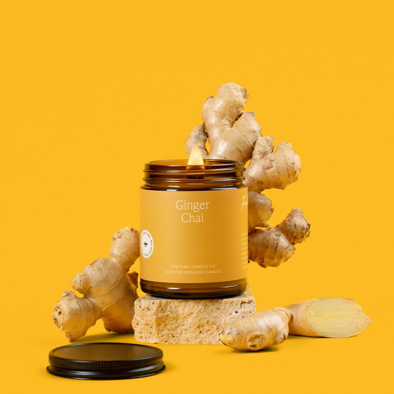 Amber glass Jar  candle of 'Ginger Chai' with ginger roots on a yellow background
