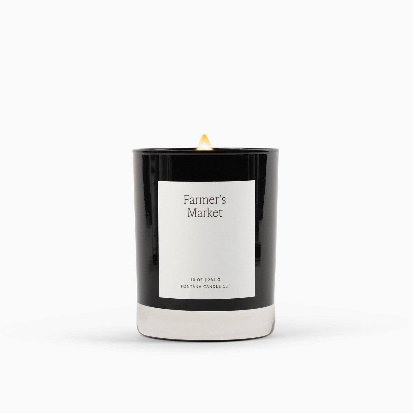 Lit black glass candle with a white label on a white background