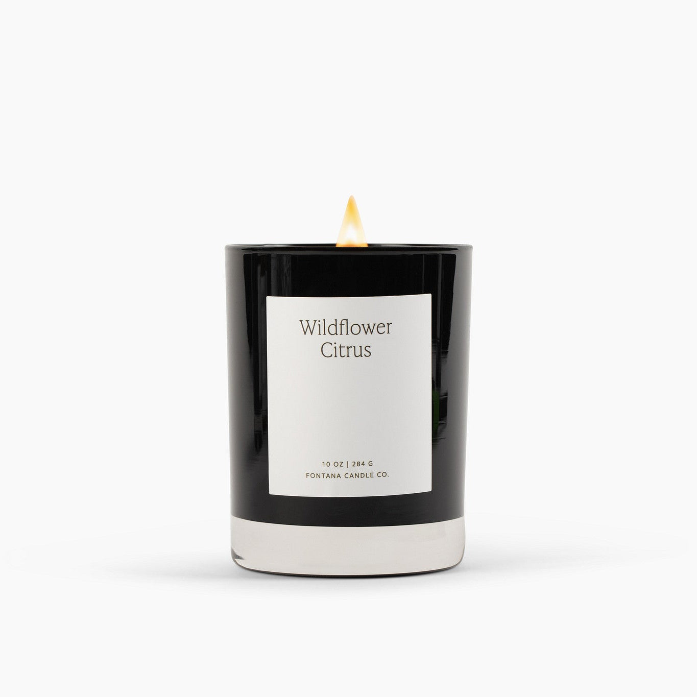 Lit black glass candle with a white label on a white background.