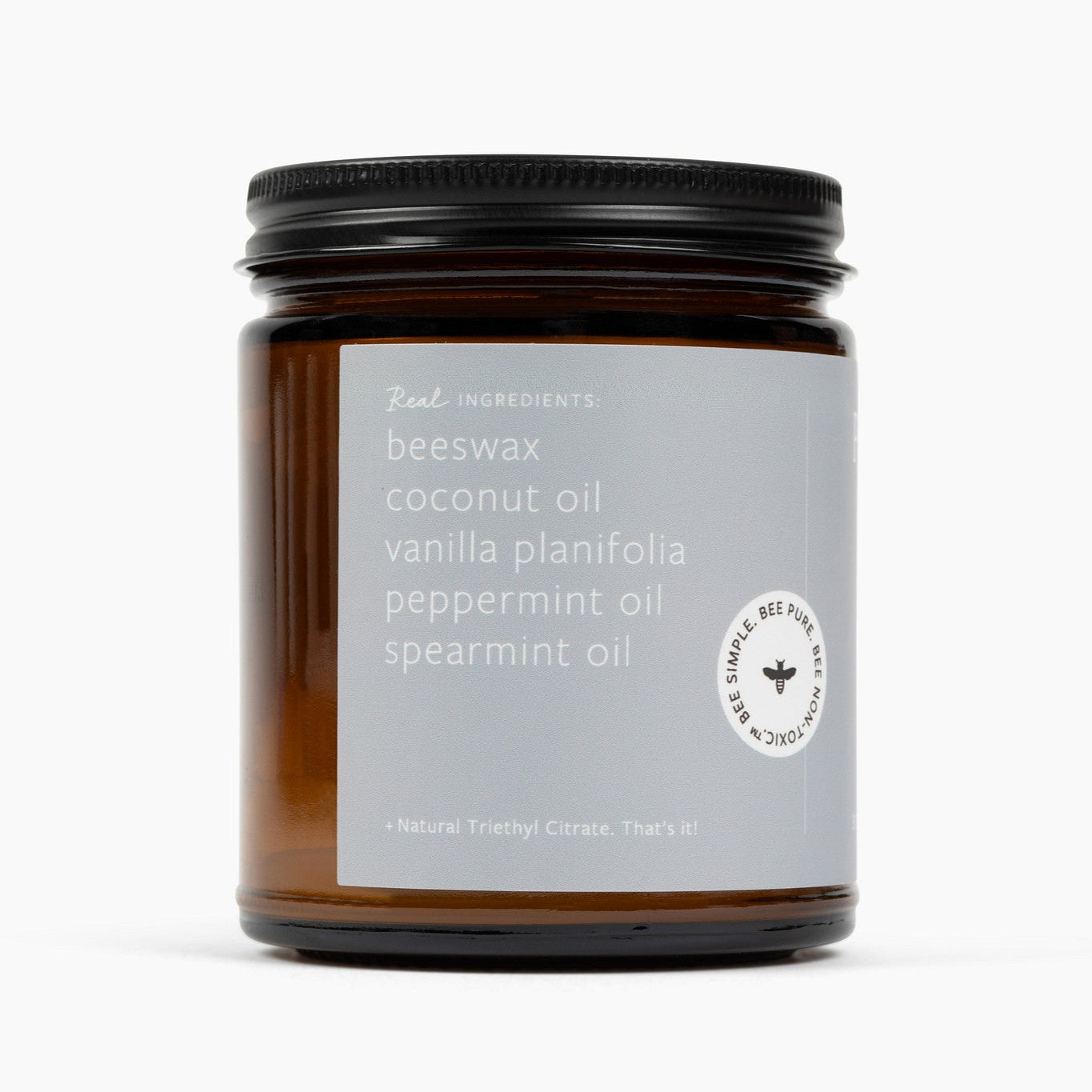Side image of an amber glass jar candle with a light gray label and the ingredient list beeswax, coconut oil, vanilla planifolia, spearmint oil, and natural triethyl citrate.
