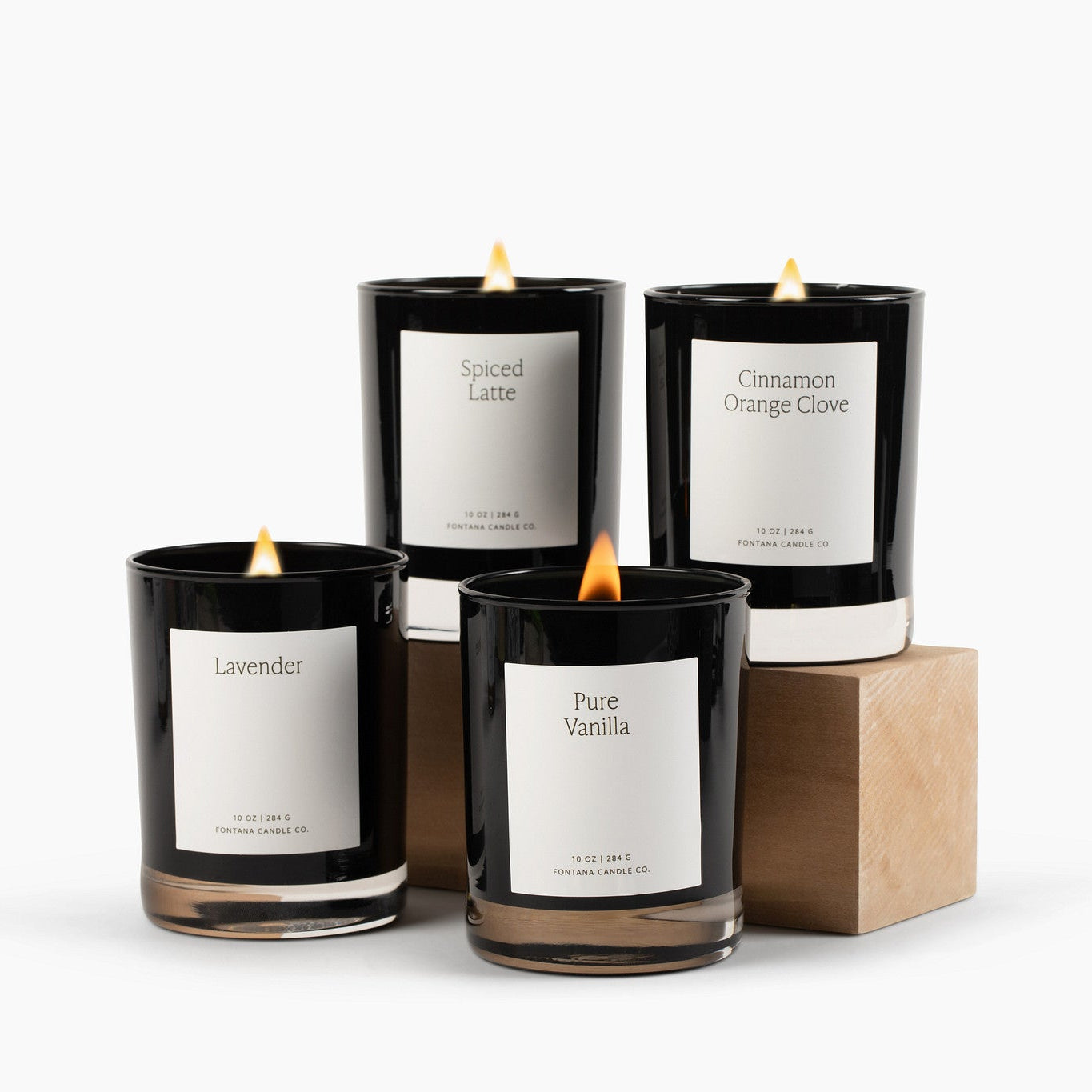 Four lit blackglass candles with white labels on a white background.