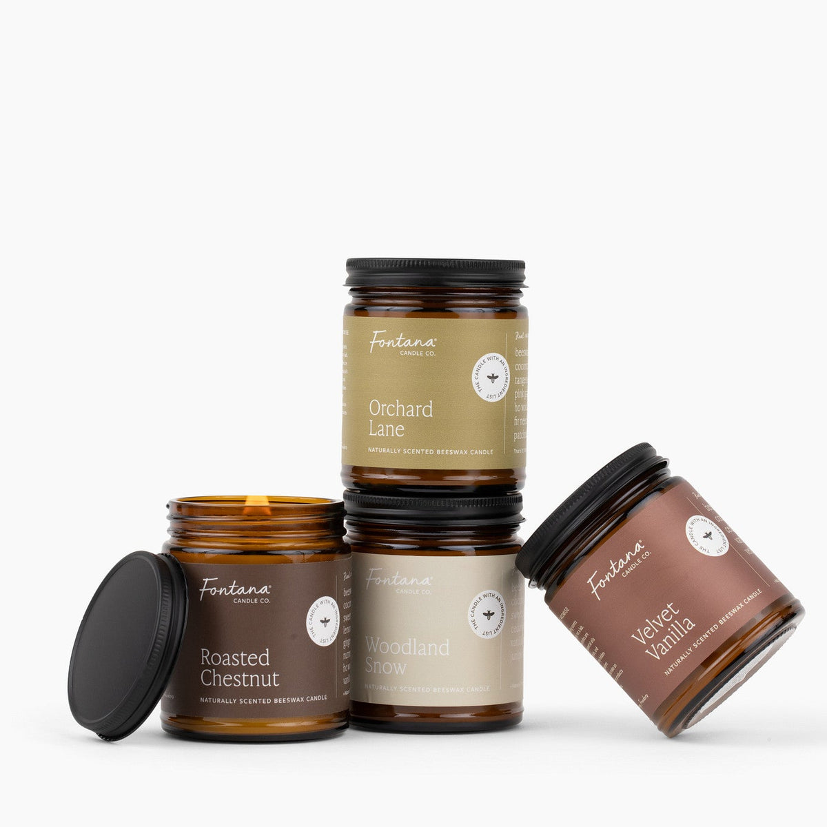 Four amber glass jar candles with brown green, and gray labels in front of a white background.