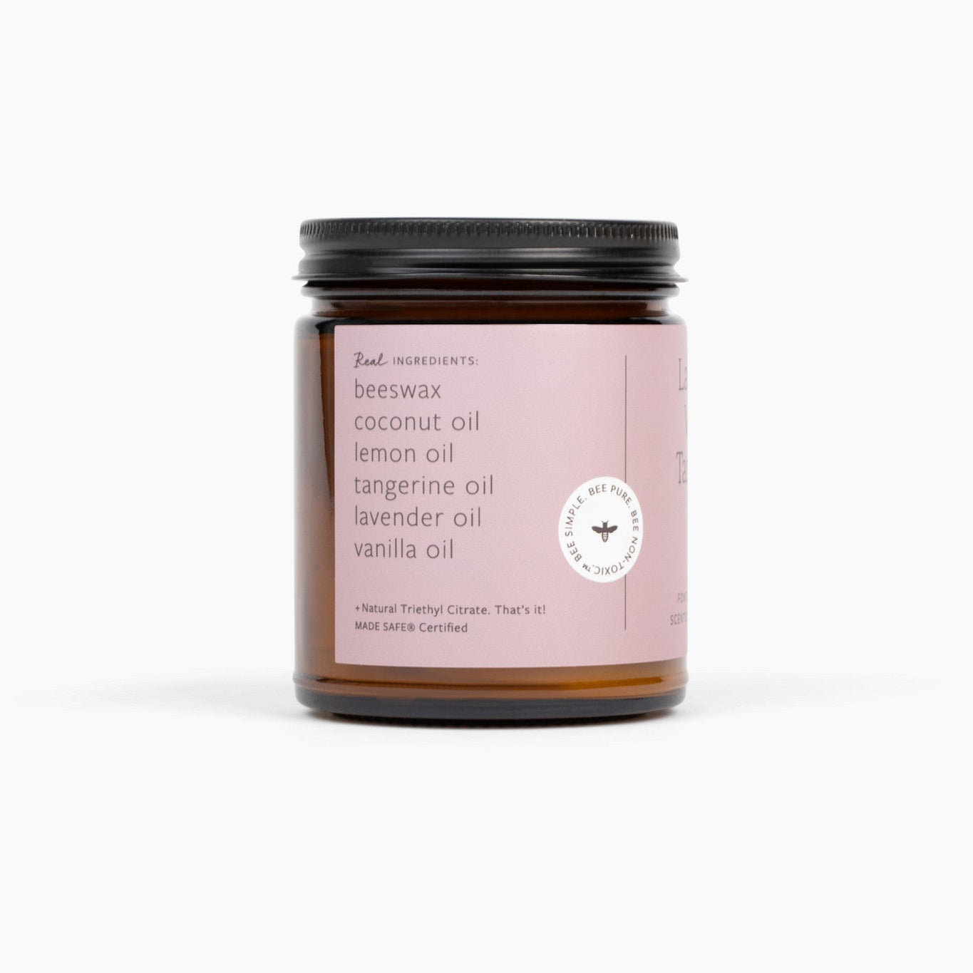 Side view of an amber glass jar candle and a black lid. The candle has a light pink label and is in front of a white background.