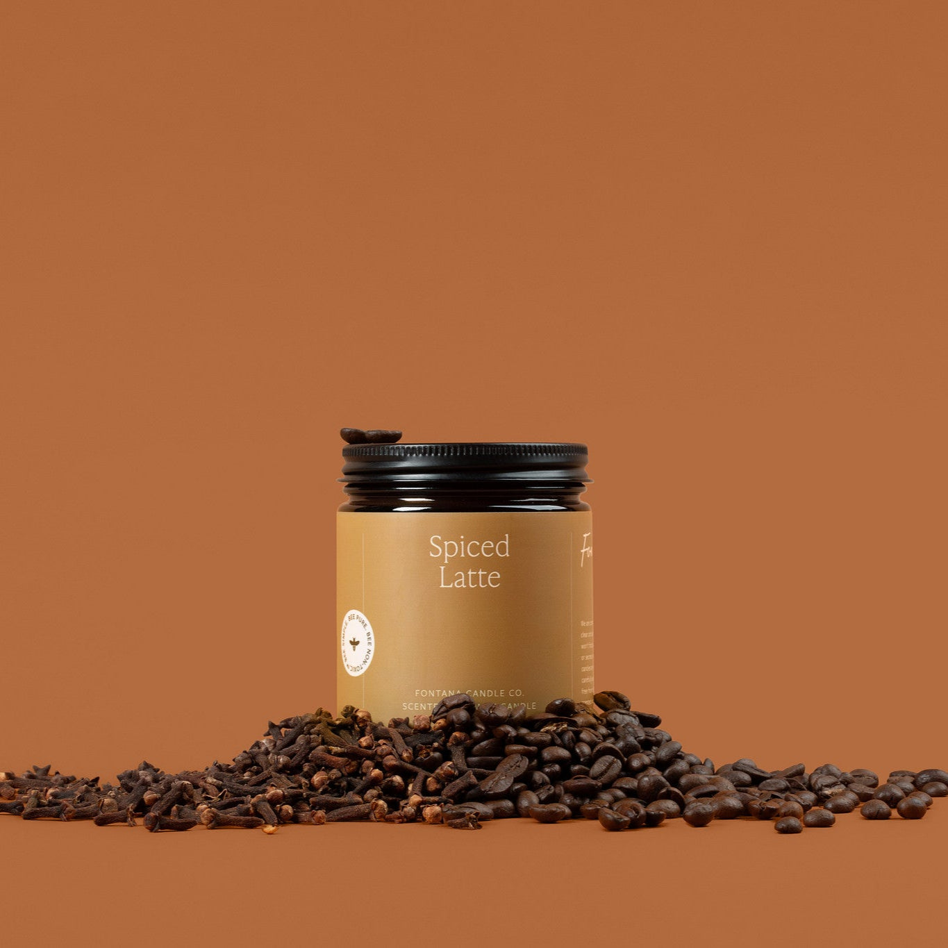 Amber glass jar of Spiced Latte with coffee beans on a brown background.