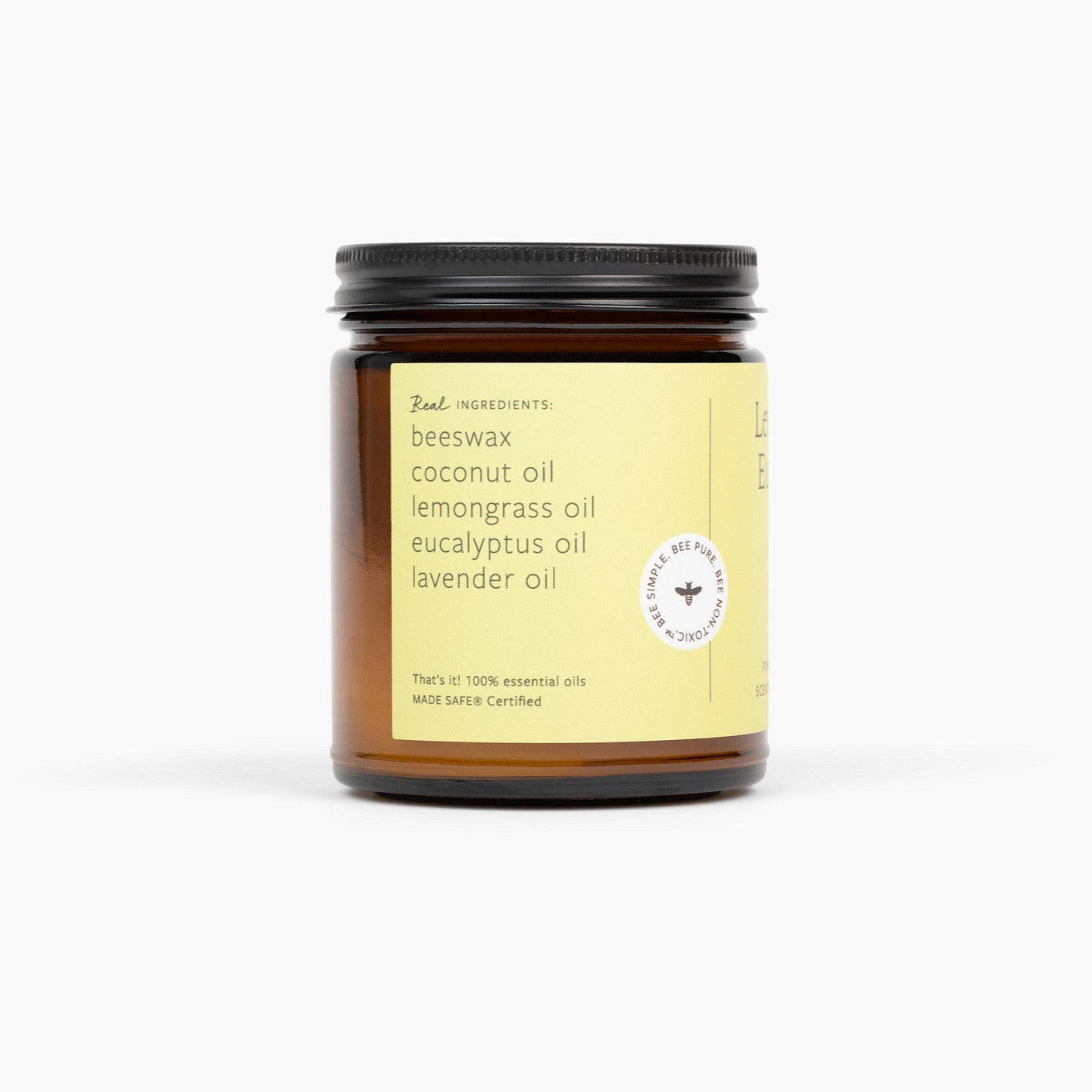 Side view of an amber glass jar candle with a black lid, light green/yellow label. The candle is in front of a white background. 
