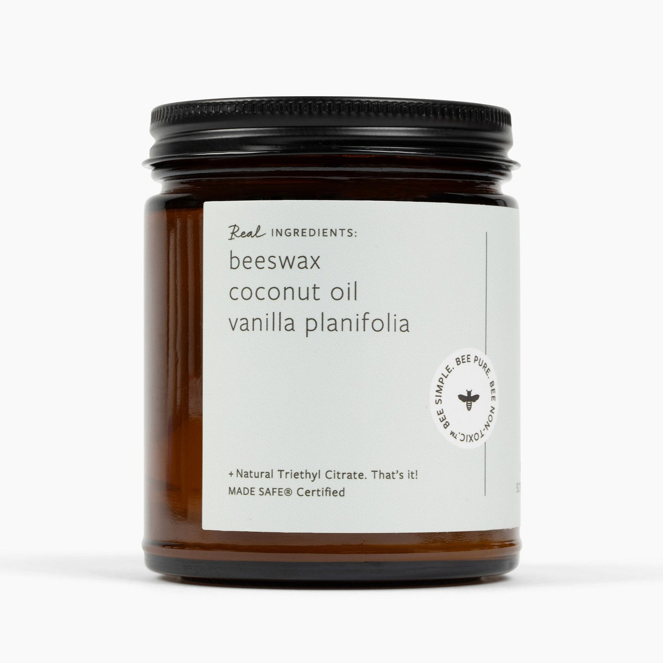 Unlit amber glass jar candle with a white label and the ingredients: beeswax, coconut oil, vanilla planifolia, and natural triethyl citrate.