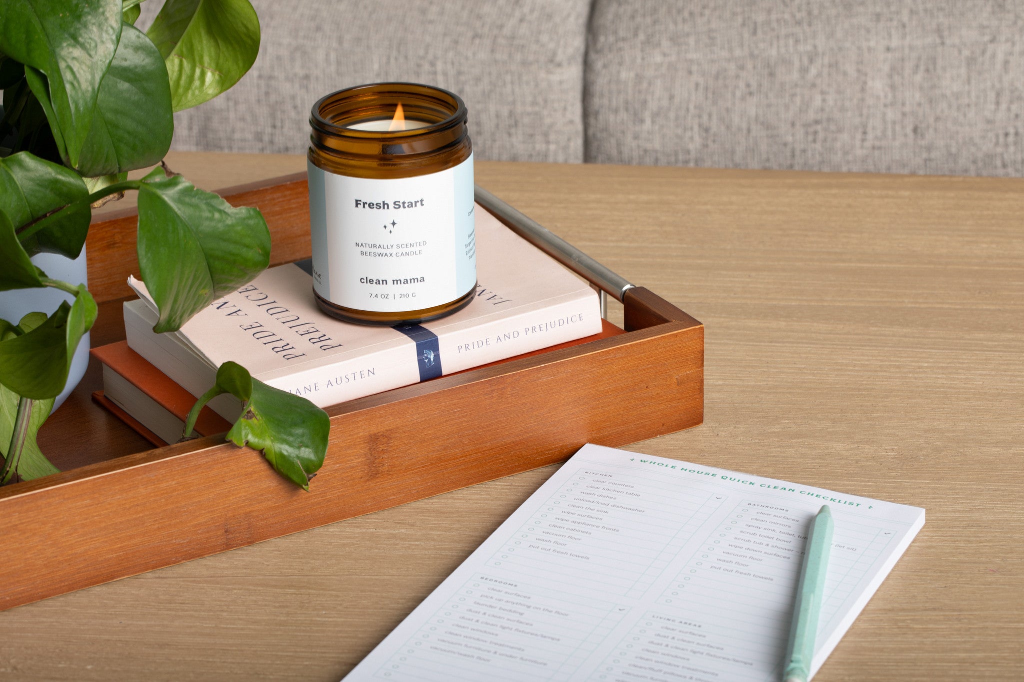 Lit 'Fresh Start' amber glass jar candle on a stack of books, next to a plant, in a living room.