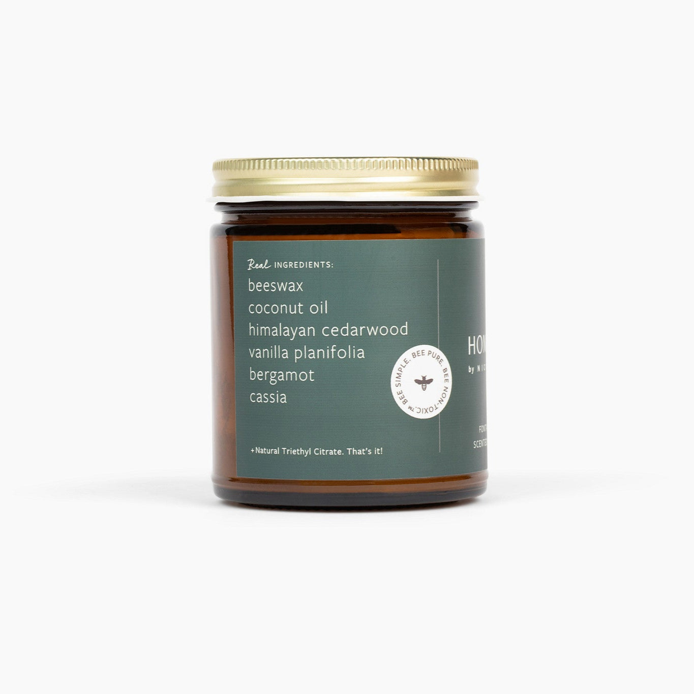 Amber glass jar candle with a gold lid, called Homewood, with a dark green label, in front of a white background.