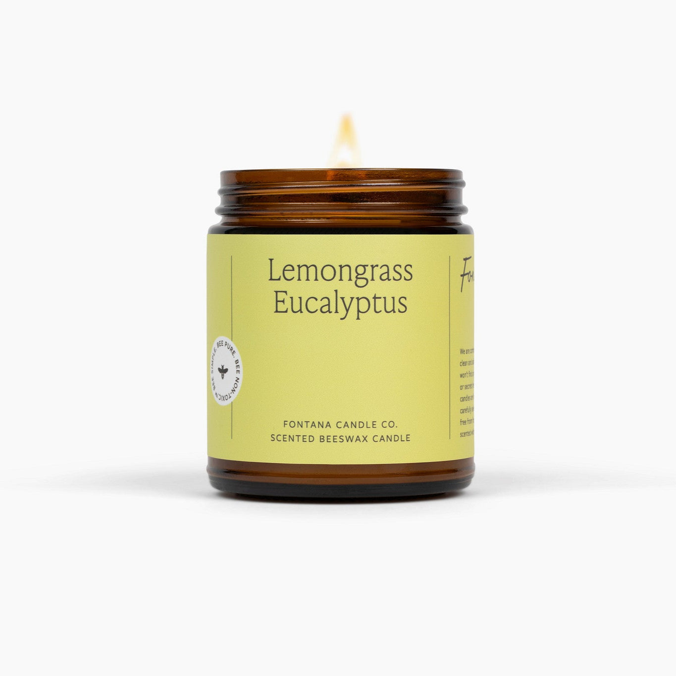 Lit amber glass jar candle with a light green/yellow label. The candle is in front of a white background. 