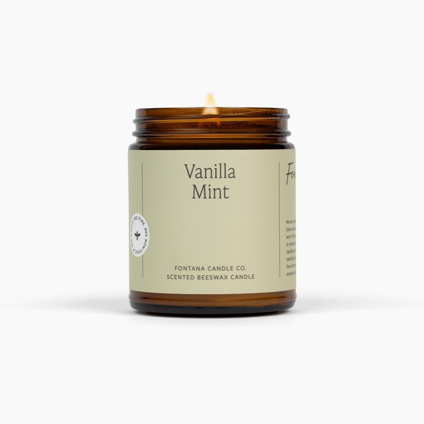 Lit amber glass jar candle with a light green label, and Vanilla Mint on the front. Candle is in front of a white background. 