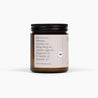 Side view of an amber glass jar candle with a black lid and a soft pink label. The candle is in front of a white background. 