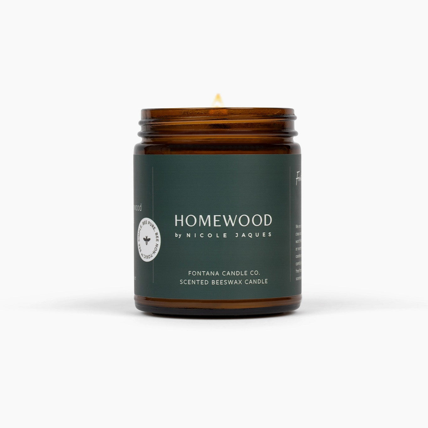 Lit amber glass jar candle called Homewood, with a dark green label, in front of a white background.