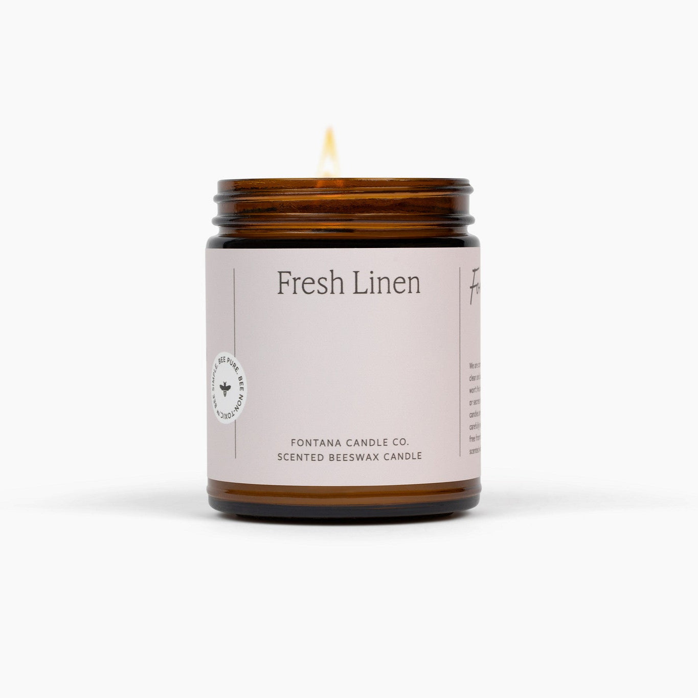 Lit amber glass jar candle with a soft pink label. The candle is in front of a white background. 