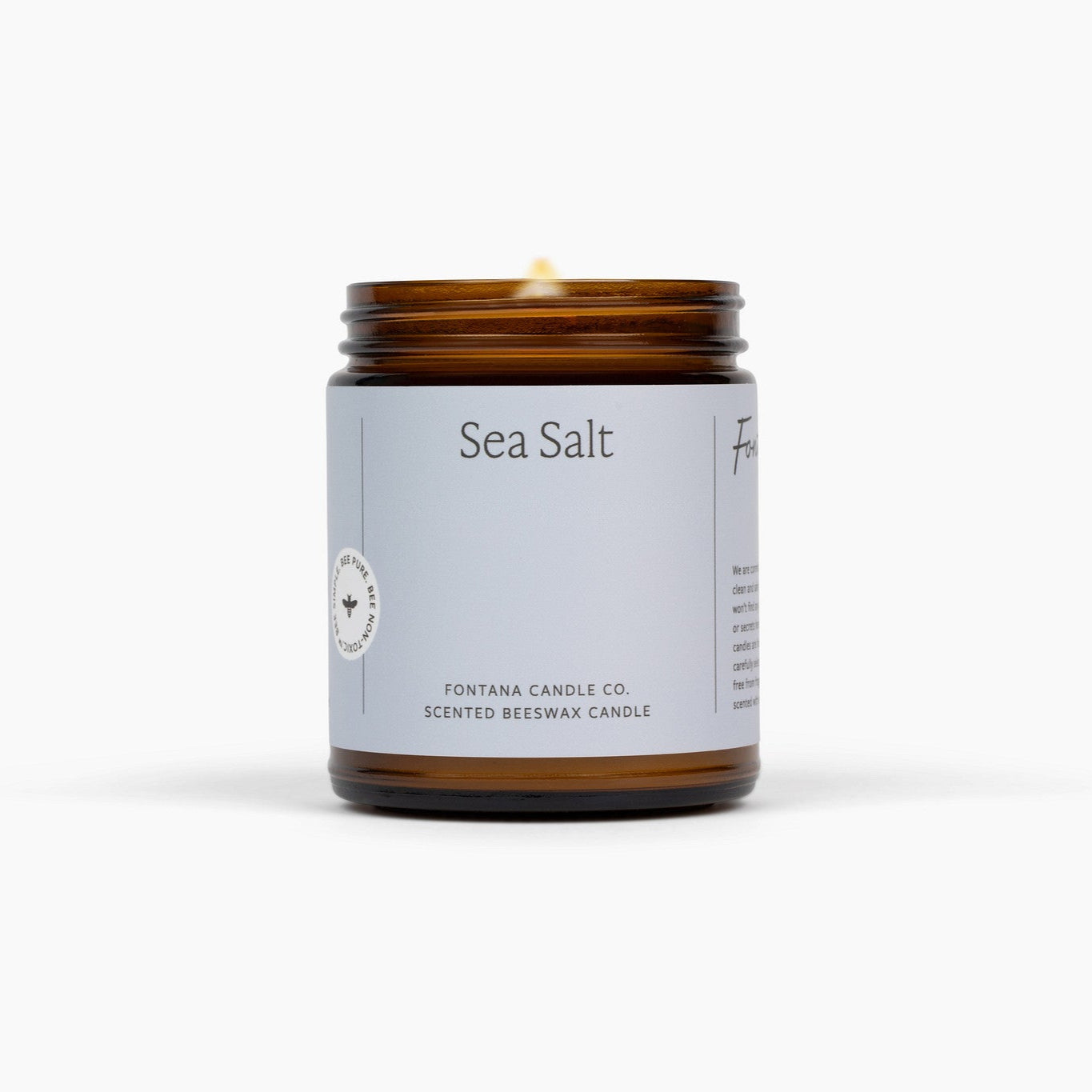 Lit amber glass jar candle with a light blue label, in front of a white background. 