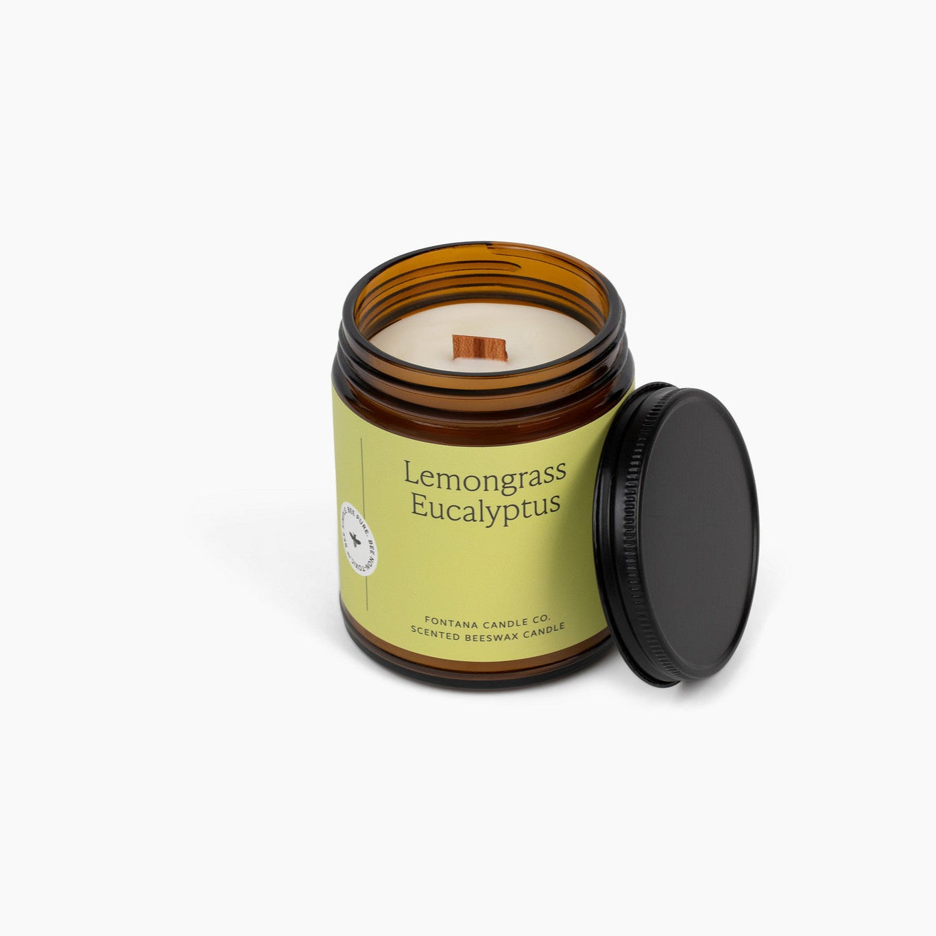 Unlit wooden wick candle in an amber glass jar and a light green label. The candle is in front of a white background. 