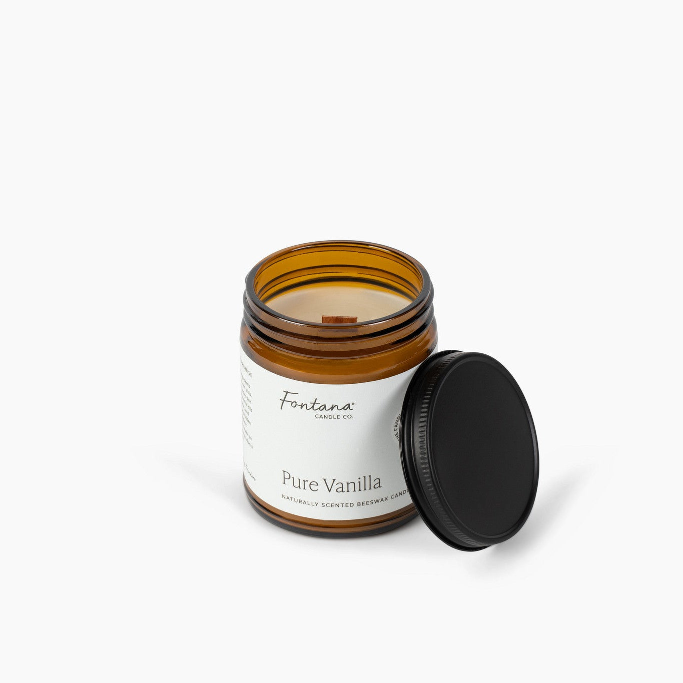 An amber glass jar candle with a white label reading 'Fontana Candle Co. Pure Vanilla' and a black screw-on lid leaning against it, photographed on a clean white background.