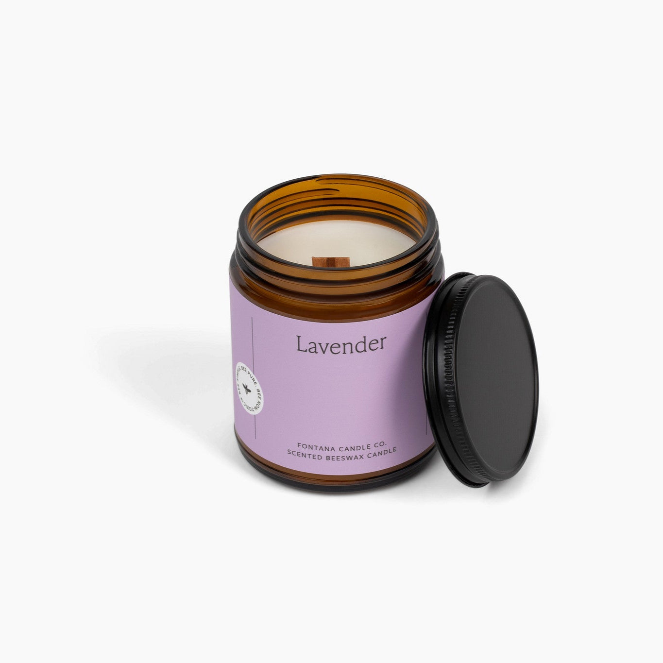 Wooden wick amber glass jar candle with a purple label. The candle is in front of a white background. 