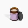 Wooden wick amber glass jar candle with a purple label. The candle is in front of a white background. 