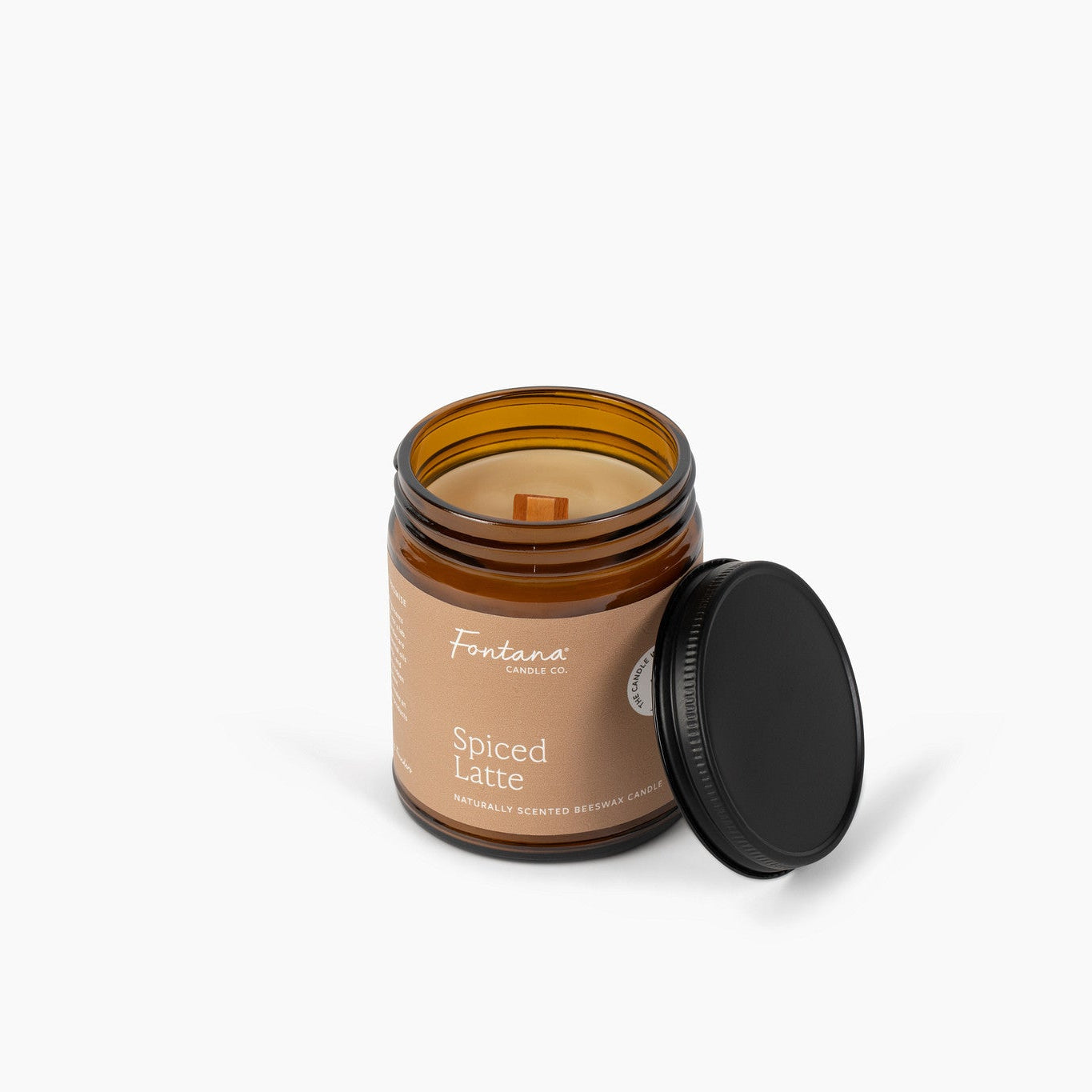 An amber glass jar candle with a black lid leaning against it on a clean white background. The brown label reads 'Spiced Latte'.
