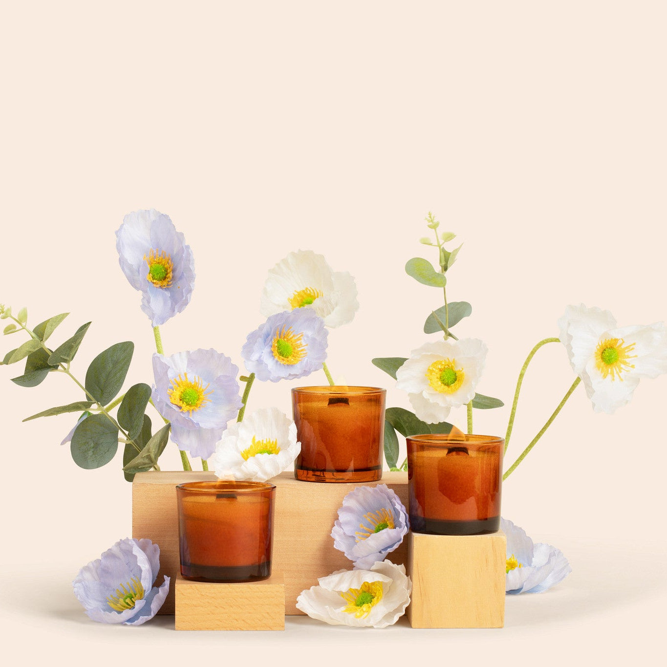 Three brown glass candles with white flowers on a beige background