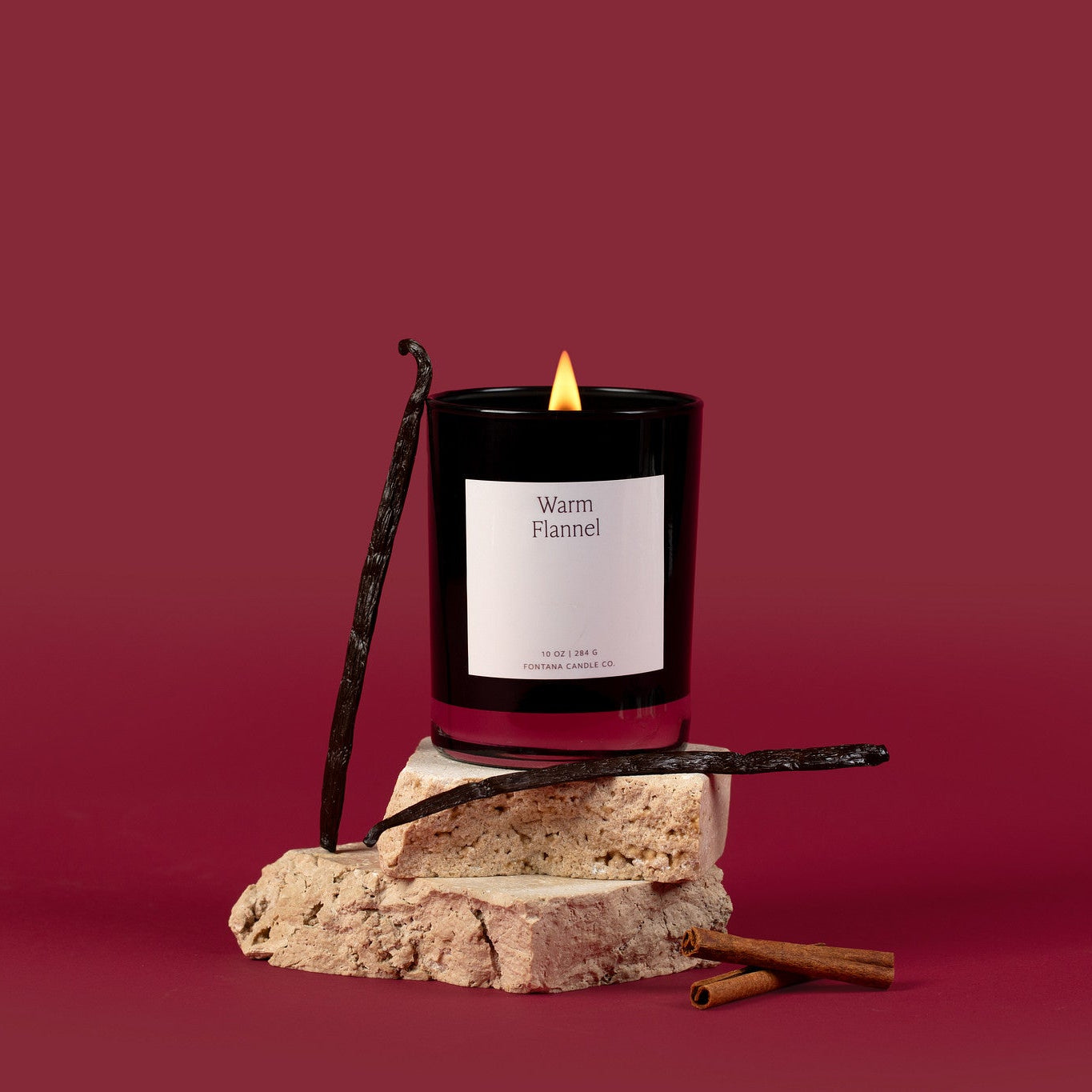 Black glass candle with a white label on a rock against a red background
