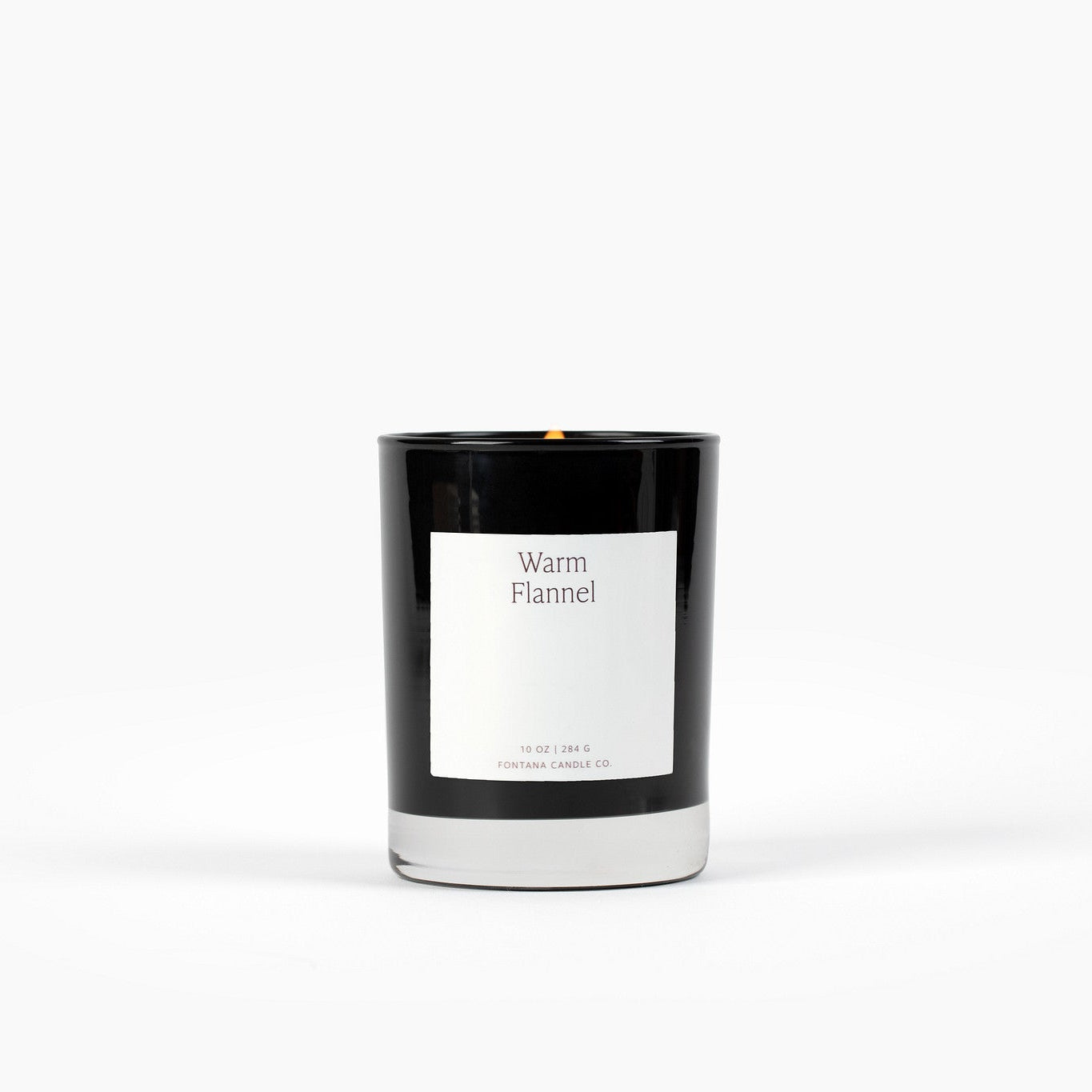 Black glass vessel candle with a minimalistic white rectangle label and the scent name Warm Flannel