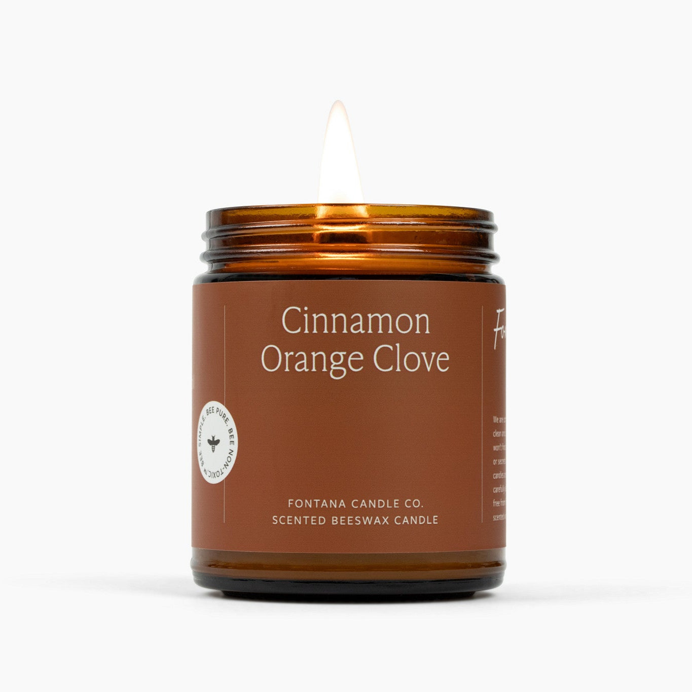 Lit amber glass jar candle with a deep orange label and Cinnamon Orange Clove scent.