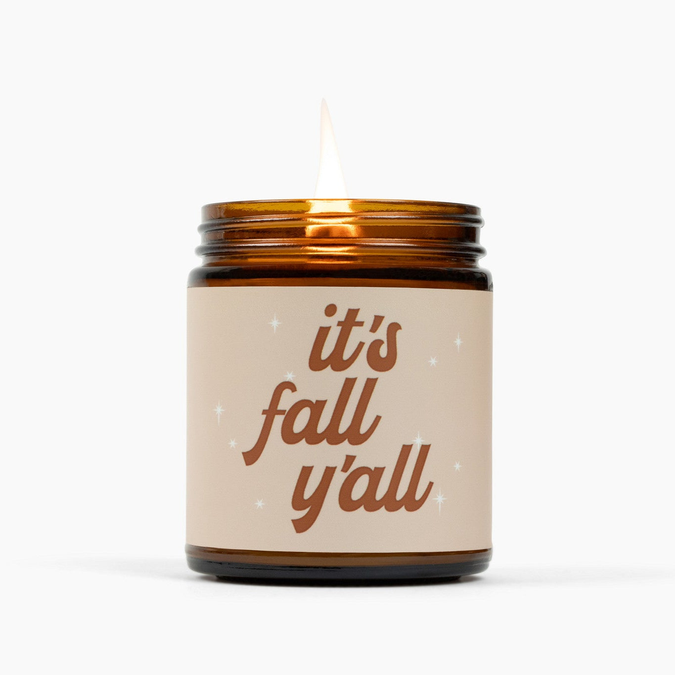 Lit amber glass jar candle with a label that says It's Fall Y'all in brown text.