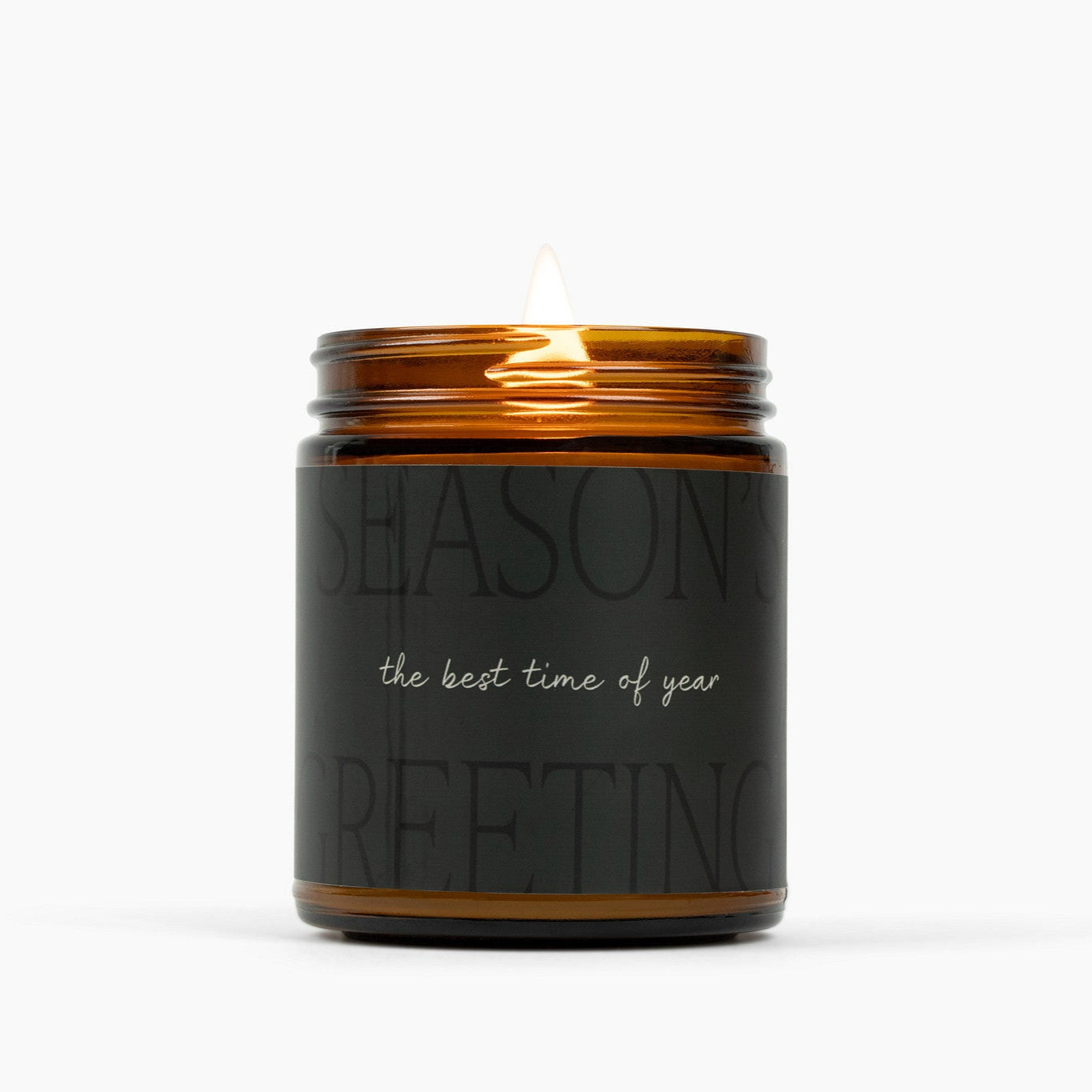 Lit amber glass jar candle with a very dark green label that says: Season's Greetings: the best time of year."