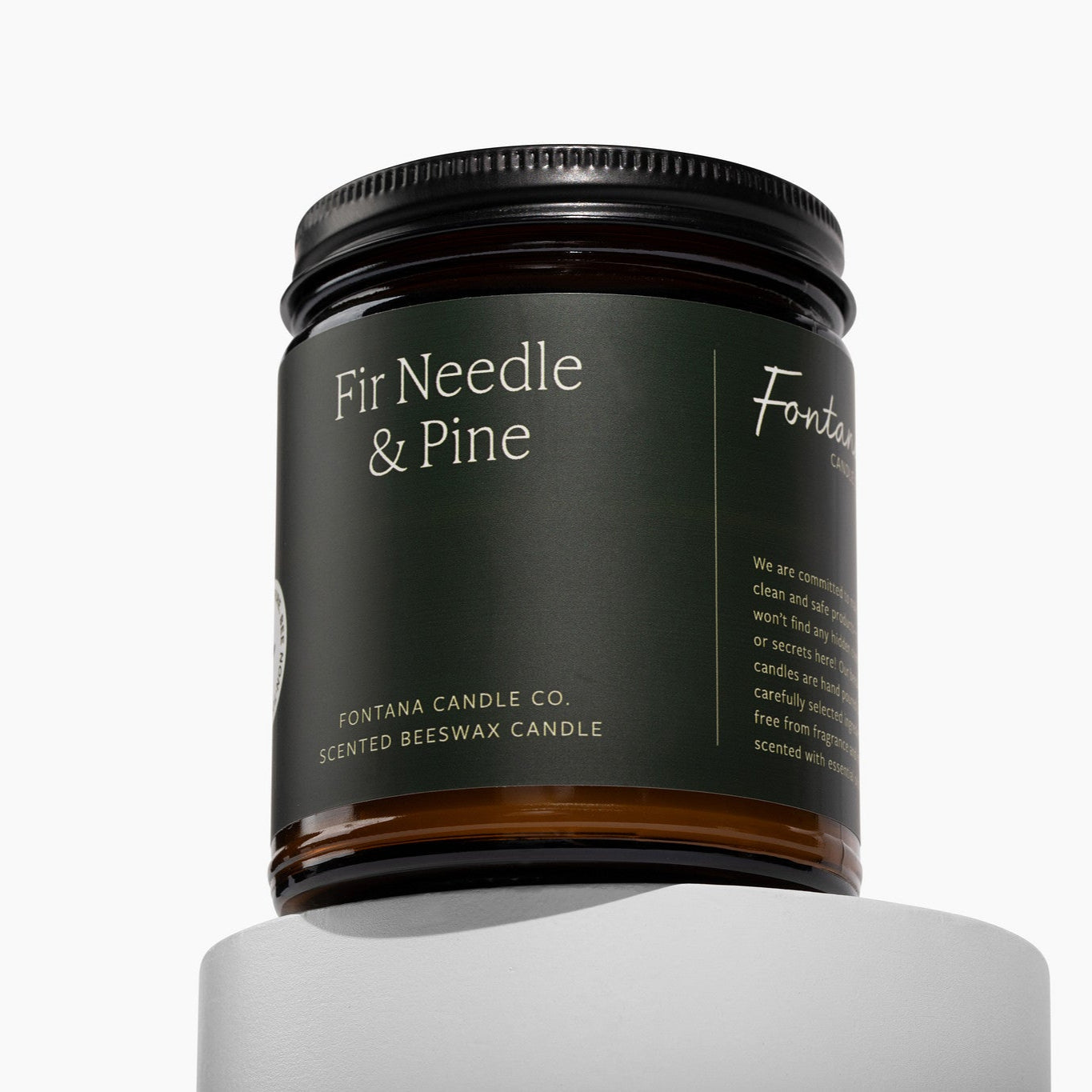 Amber glass jar candle with a green label. It is labeled 'Fir Needle & Pine' by Fontana Candle Co. on a white background