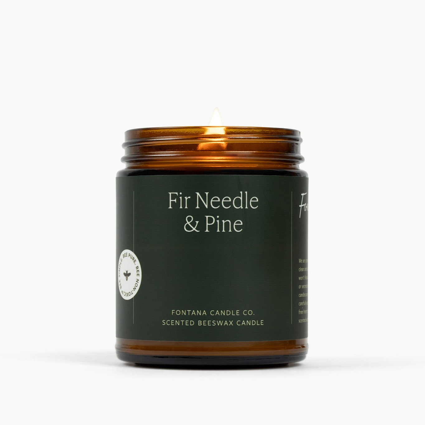 Lit amber glass jar candle with a dark green label and Fir Needle & Pine scent.