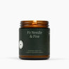 Lit amber glass jar candle with a dark green label and Fir Needle & Pine scent.