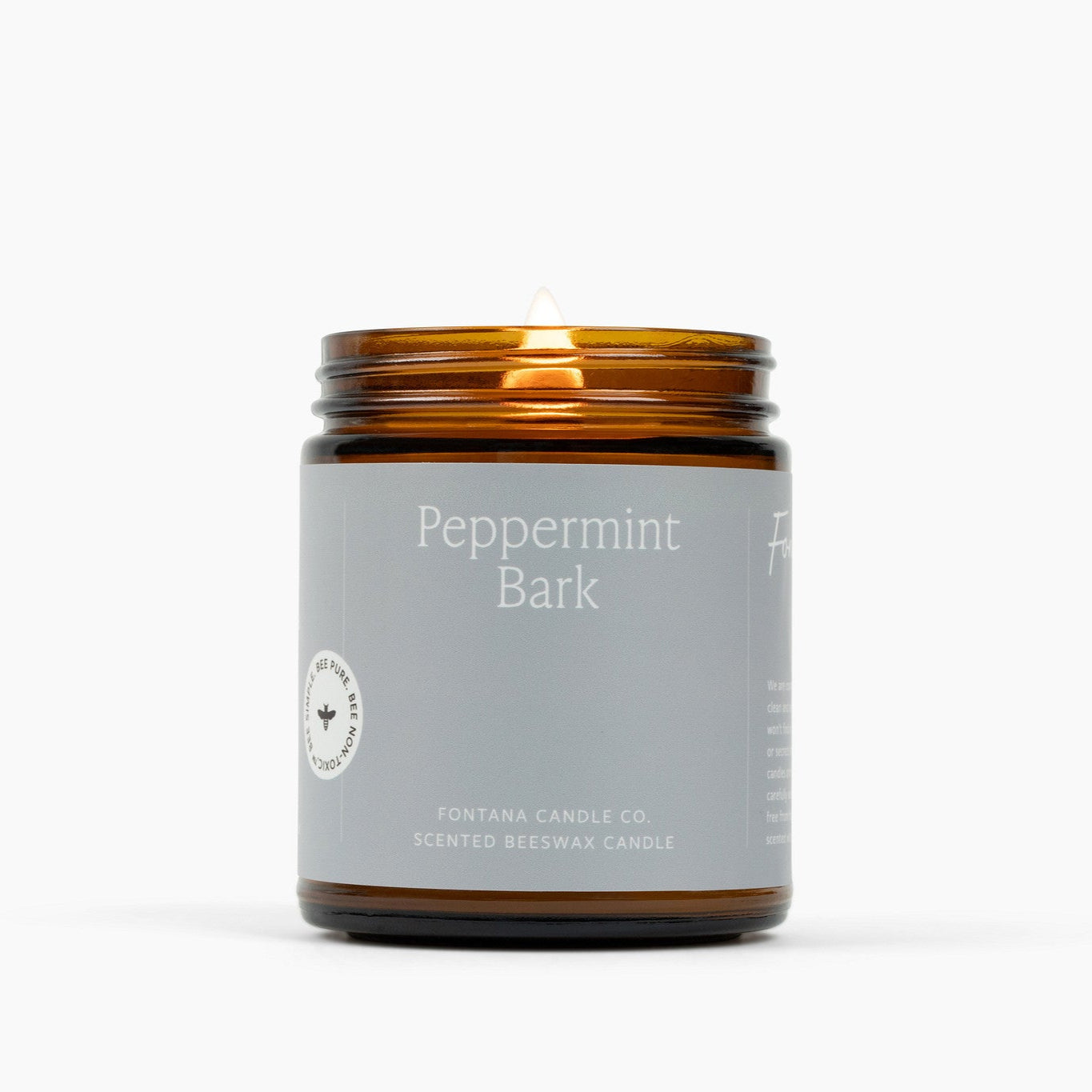 Lit jamber glass jar candle with a light gray label and the scent Peppermint Bark.