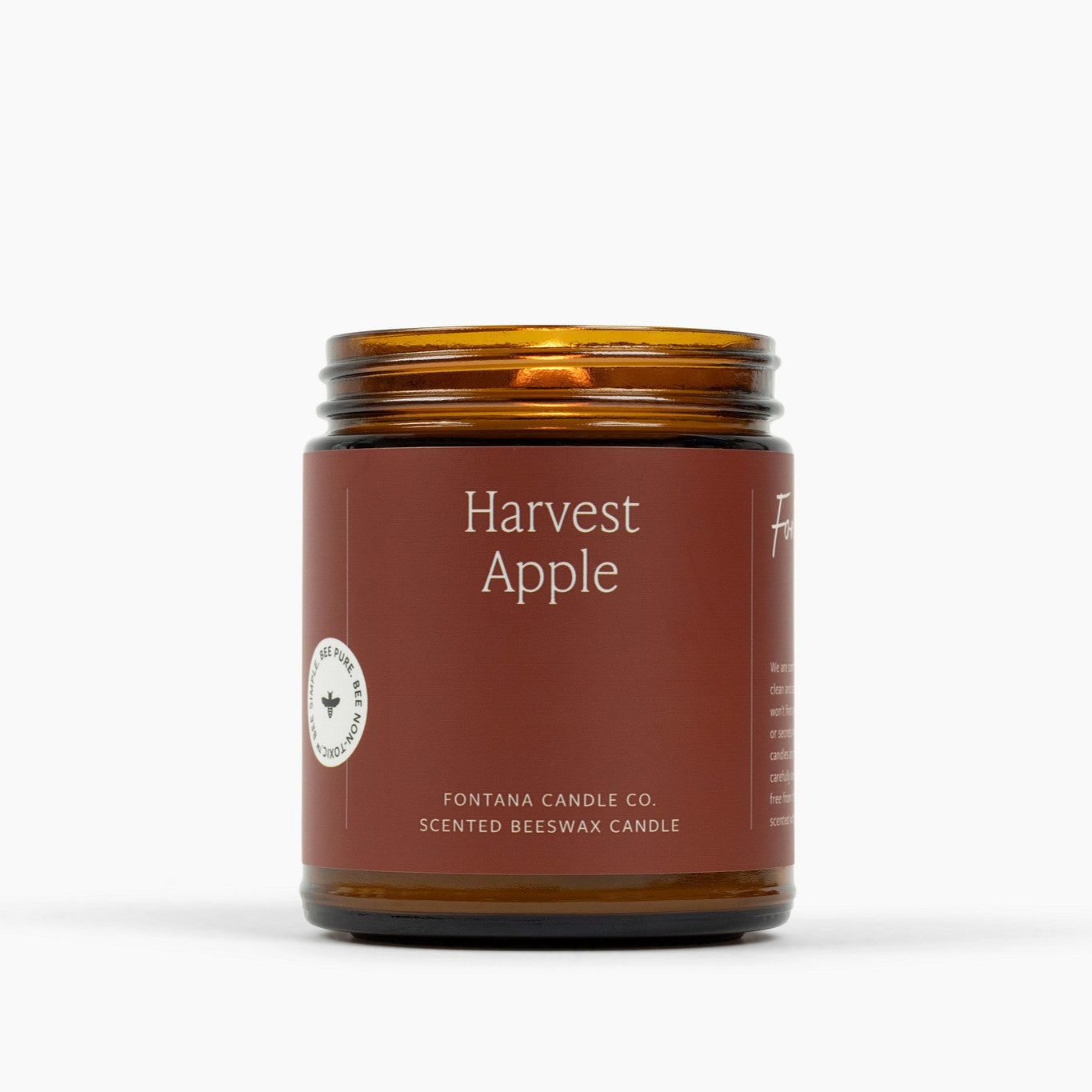 Lit amber glass jar candle with a deep red label and Harvest Apple scent.